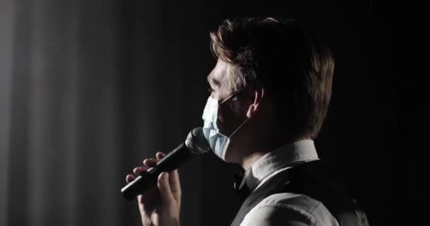 Man gastheer van evenement in medisch masker spreekt op microfoon bij concert op het podium. — Stockvideo