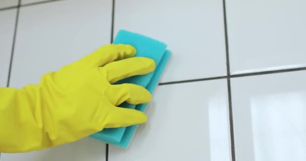 Hand einer Person in gelbem Handschuh wäscht weiße Fliese mit blauem Schwamm. — Stockvideo