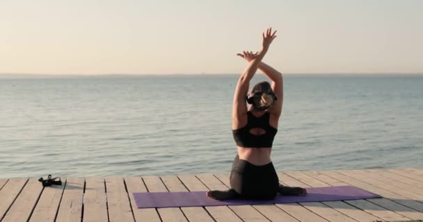 Yoga yapan kadın nehir rıhtımında mindere oturup yan yatarak esneme hareketleri yapıyor.. — Stok video