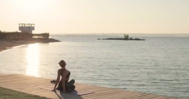 Yoga yapan kadın nehir rıhtımında bacak ve omurga esnetiyor..