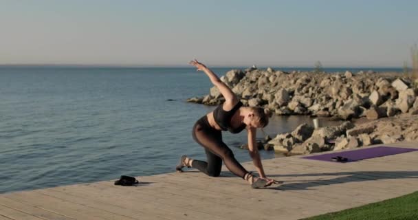 Sportig flexibel kvinna gör längsgående split sitter på piren nära floden. — Stockvideo