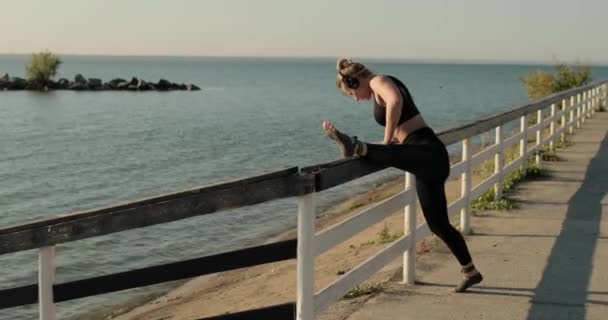 Ung kvinna sträcker på benet sätter den på staketet vid flodstranden.. — Stockvideo