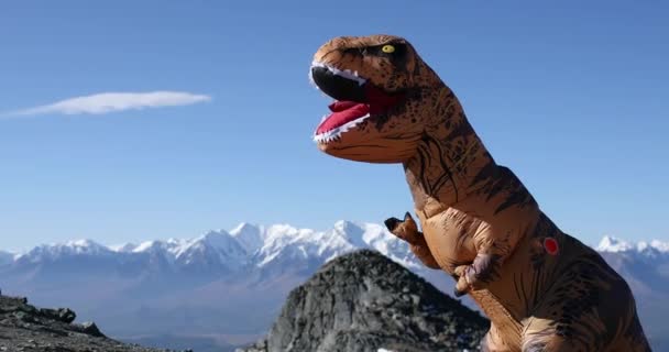 Riesige Dinosaurierpuppe Tyrannosaurus Rex mit Person im Inneren in Gebirgswellen Händen. — Stockvideo