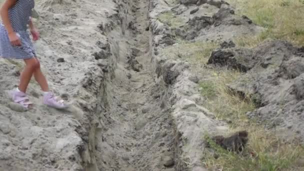Két kis lányok átugrani egy földes árok ásott szóló csövek. — Stock videók