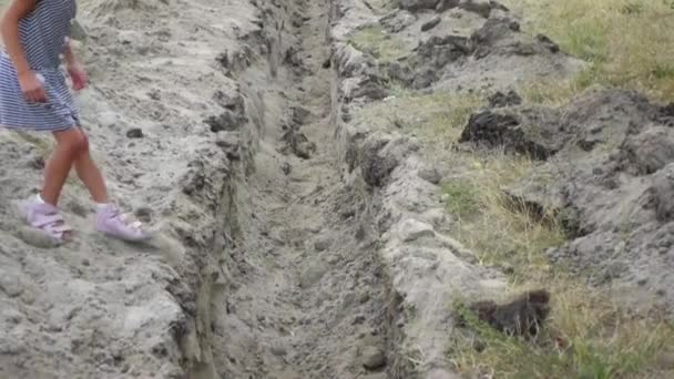 Two little girls jump over an earthen ditch, dug for laying pipes. — Stock Footage Two little girls jump over an earthen ditch, dug for laying pipes. Stock Video