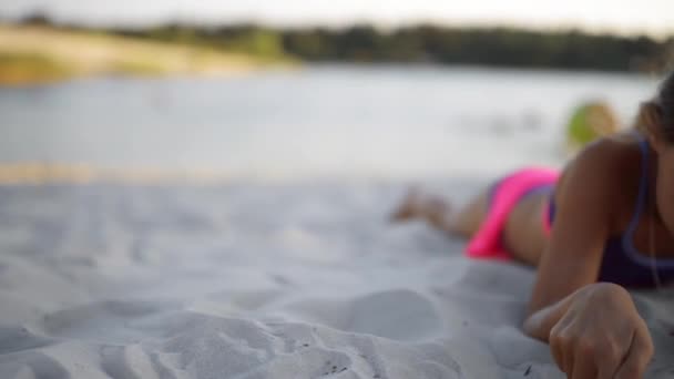 Piccola bella ragazza si trova sulla sabbia bianca della grande spiaggia del lago . — Video Stock