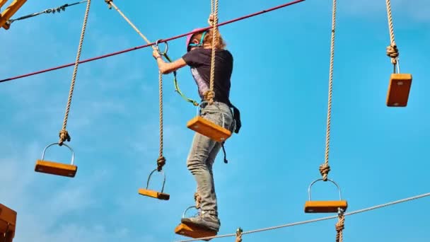 Mädchen-Klettern im Abenteuerpark ist ein Ort, der eine Vielzahl von Elementen enthalten kann, wie Seilkletterübungen, Hindernisparcours und Seilrutschen. — Stockvideo