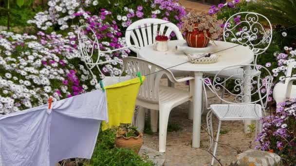 床上用品 在花园花卉和塑料桌椅的背景下洗涤后晾干 — 图库视频影像
