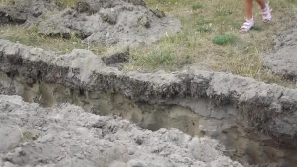 Little girl jumps over an earthen ditch, dug for laying pipes. — Stock Footage Little Girl Jumps Earthen Ditch Dug Laying Pipes Stock Footage