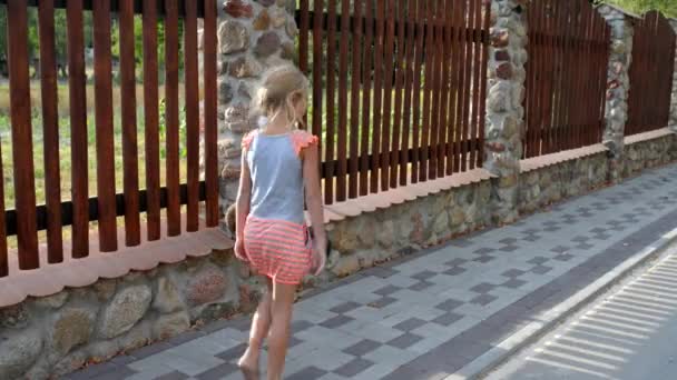 Small beautiful girl walks along tall wooden fence. — Stock Video