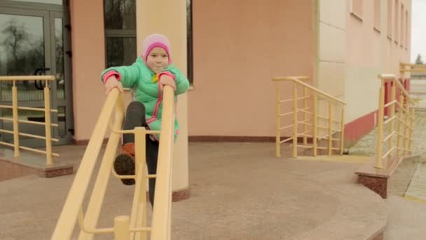 Kleines hübsches Mädchen in Herbstjacke klettert auf Metallgeländer am Gebäude — Stockvideo