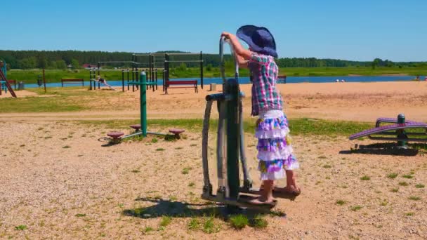 Niña se dedica a simulador de deportes de metal cerca de la playa con lago . — Vídeos de Stock