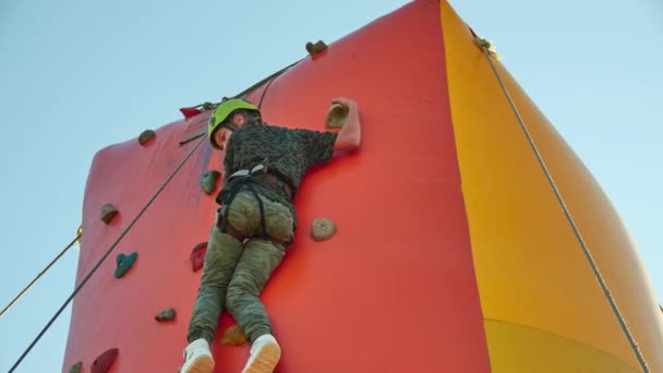 Chica en casco sube a la pared de escalada. La pared de escalada es una pared construida artificialmente con agarres para manos y pies . — Vídeos de Stock