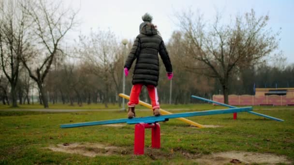 Kleines Mädchen in Jacke reitet auf Schaukel im herbstlichen Stadtpark. — Stockvideo