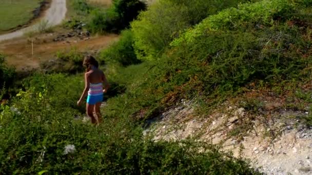 Kleine mooi meisje in zwembroek afdaalt berg met lage struiken in Kroatië. — Stockvideo