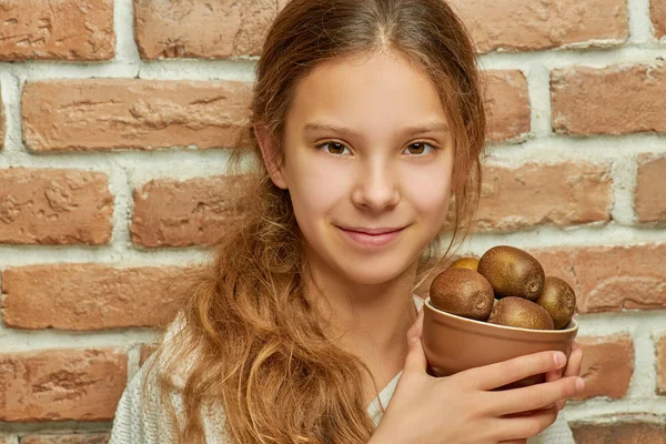 Dospívající Dívka Dlouhými Vlasy Drží Desku Kiwi Pozadí Cihlová Zeď — Stock fotografie