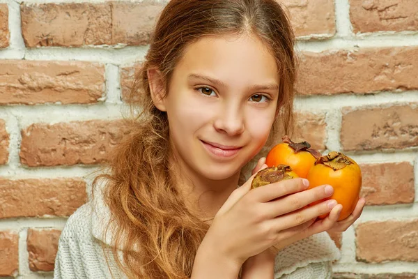 Tonåring Flicka Med Långt Hår Håller Persimon Bakgrund Tegelvägg — Stockfoto