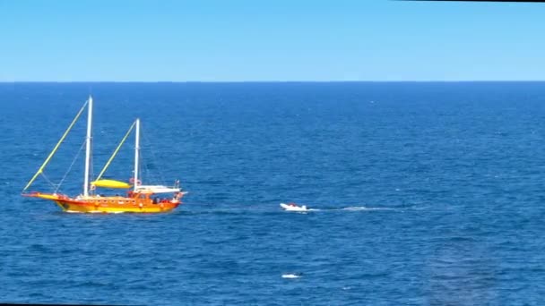 Kleine Jacht mit abgesenktem Boot zieht auf See nahe felsiger Küste. — Stockvideo