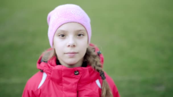ピンクの帽子と緑の背景に手を振る赤いジャケットの美しい少女 — ストック動画