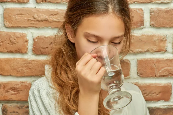 Little girl drinking water against brick wall — Stock Photo, Image