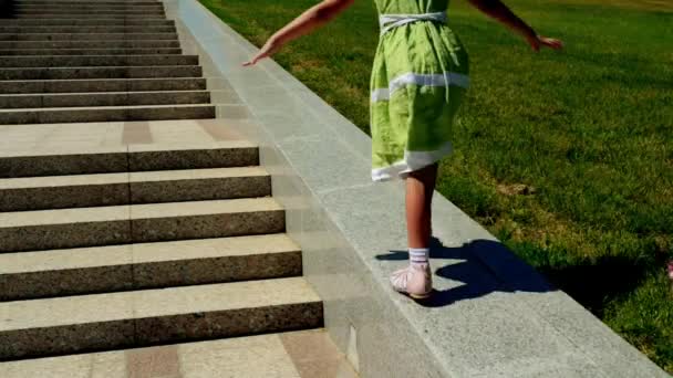Two little sister girls walk along parapet on large granite staircase in summer city garden — Stock Video