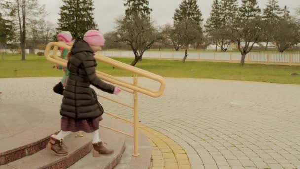 Deux belles petites filles courent sur les escaliers près des mains courantes en métal jaune . — Video