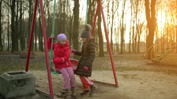 Dos hermosas niñas en columpio en el parque de otoño de la ciudad . — Vídeos de Stock