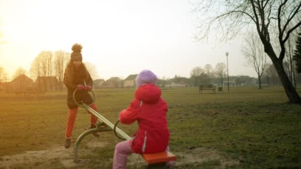 Zwei hübsche kleine Mädchen auf Schaukel im herbstlichen Stadtpark. — Stockvideo