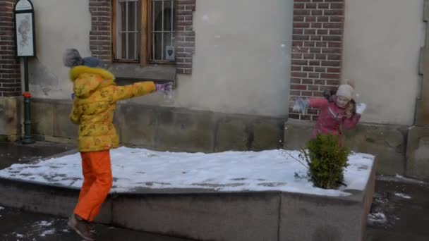 Twee kleine meisjes in winter kostuums spelen sneeuwballen in de buurt van oud gebouw. — Stockvideo