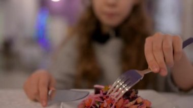 Güzel genç kız çatal ve bıçak kullanarak büyük kafede salata salata yiyor.