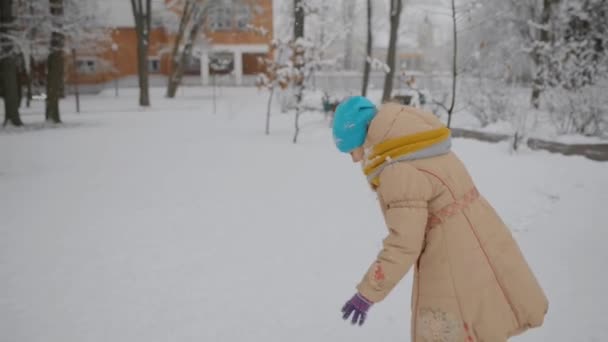 ベージュのジャケットの小さな美しい女の子は雪玉を彫刻し 冬の都市公園でそれらを投げます — ストック動画