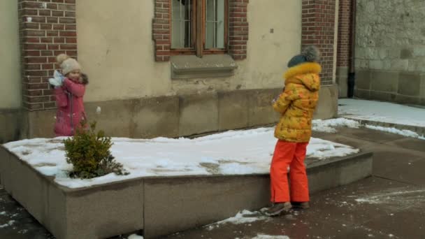 Две Маленькие Девочки Зимних Костюмах Играют Снежки Возле Старого Здания — стоковое видео