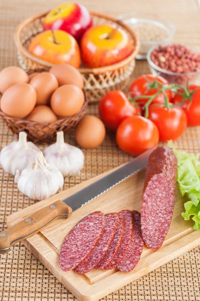 Tasty Sausage Knife Lying Cutting Board Wicker Basket Apples Garlic — Stock Photo, Image