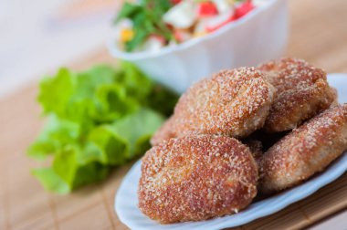 Bambu masa örtüsünün üzerinde beyaz bir tabakta kızarmış domuz köftesi. Arka planda, yengeç salatası..