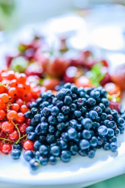 Yaban mersini, kırmızı kuşüzümü ve çilek ve beyaz bir tabakta yakın plan.