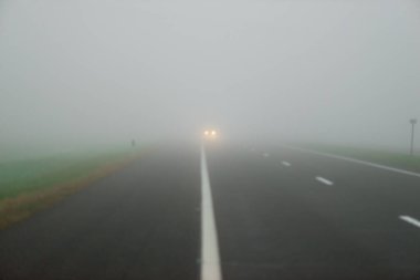 Sabah sisinde asfalt yolda. Parlayan ışıkları olan arabaların yanından geçerken.