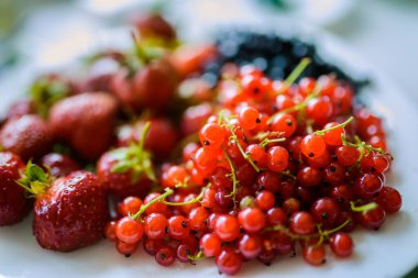 Beyaz bir tabakta kırmızı üzümler, çilekler ve yabanmersinleri..