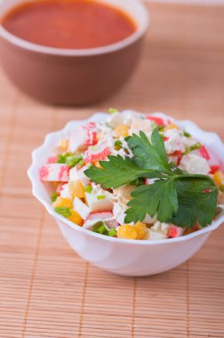 Yengeç çubuklu salata, tabakta mısır ve maydanoz ve bambu masa örtüsünde Rus çorbası..