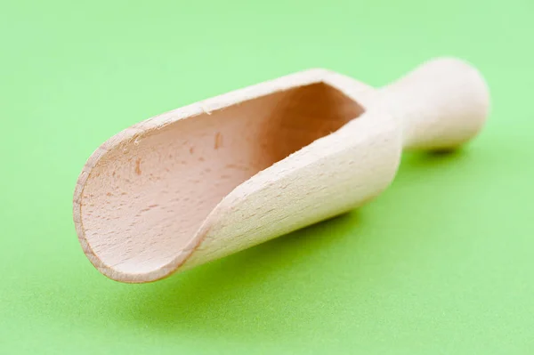 Wooden measuring scoop for flour and cereals on a green background.