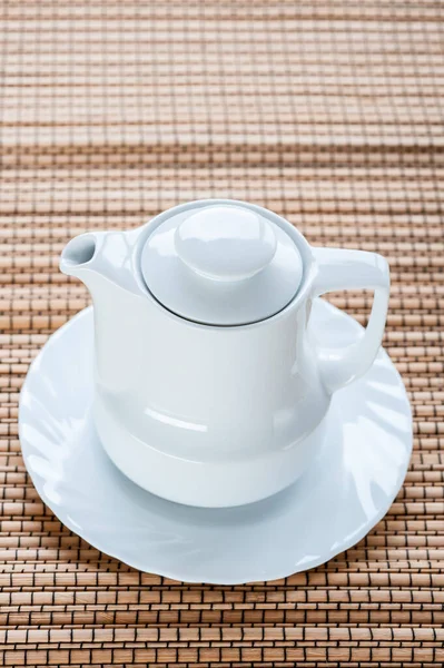 有茶托的白色小茶壶正立在竹桌布上 — 图库照片