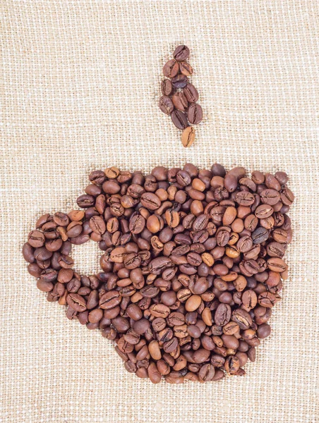 黄麻布の背景にカップの形でコーヒー豆 — ストック写真