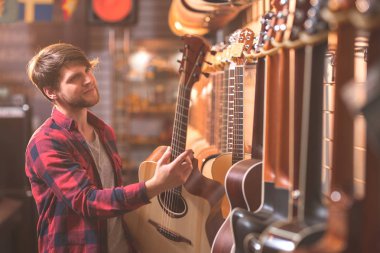 Genç müzisyen bir müzik mağazasında bir gitar seçimi