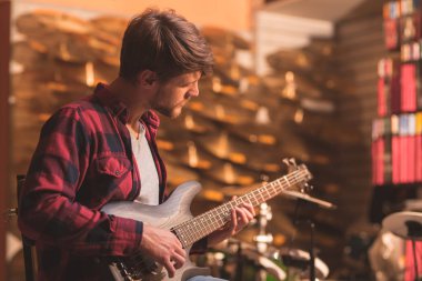 Genç adam bir mağazada bas gitar çalmaya