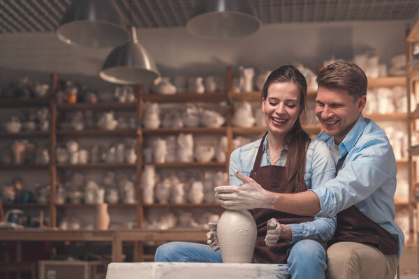 Smiling couple behind a potter's wheel in pottery