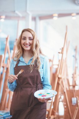 Sanatçı sanat deposundaki bir paletle gülümseyen