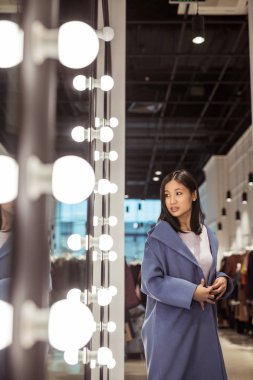 Genç kadın bir ceket, bir mağaza aynaya