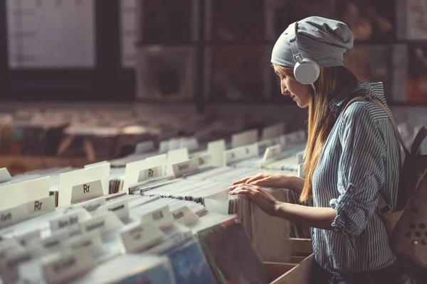 ヘッドフォンの音楽ストア内のレコードの参照を持つ少女 — ストック写真