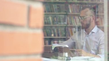 Genç adam bir kitaplıkta yazarak