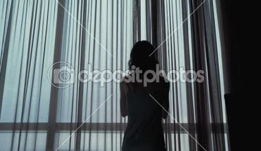 Çekici kız pencerede perdeleri açar 