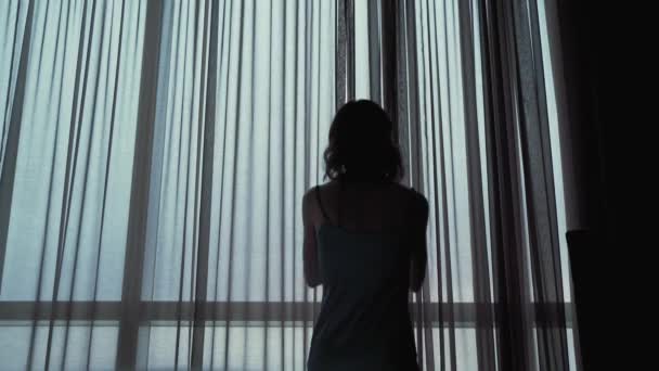 Menina atraente abre as cortinas na janela — Vídeo de Stock